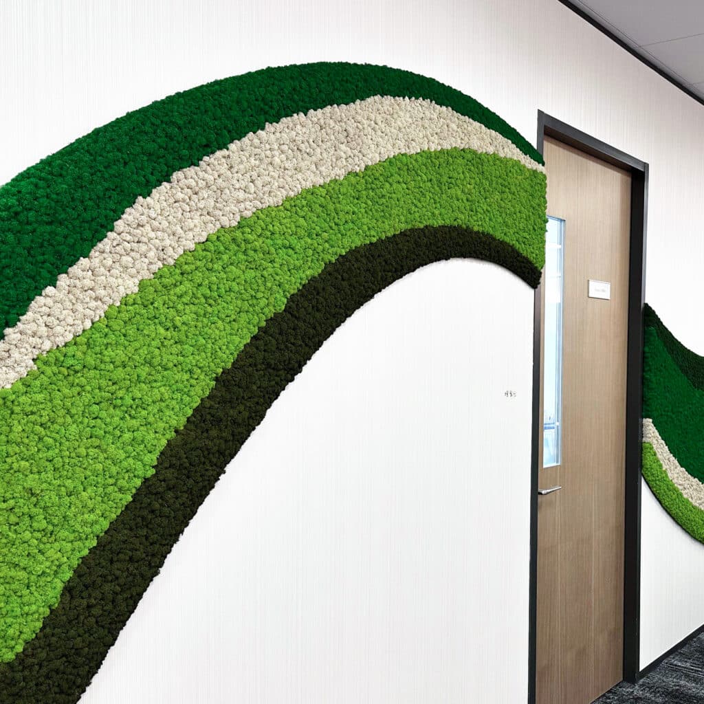 Reference image of Polarmoss Ltd. Office interior with large custom made colored moss element reaching through the whole wall. Shape of a wave. Four different colors of moss used. Produced by Polarmoss.